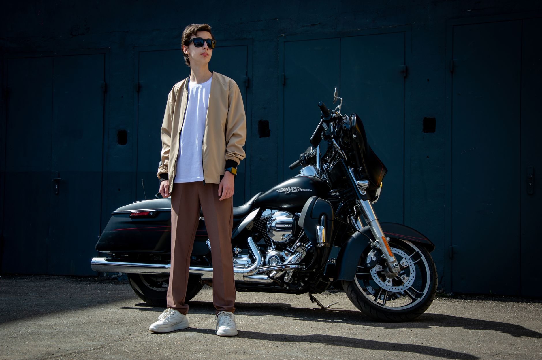 Man in casual fashion poses with motorcycle outdoors, showing urban style.