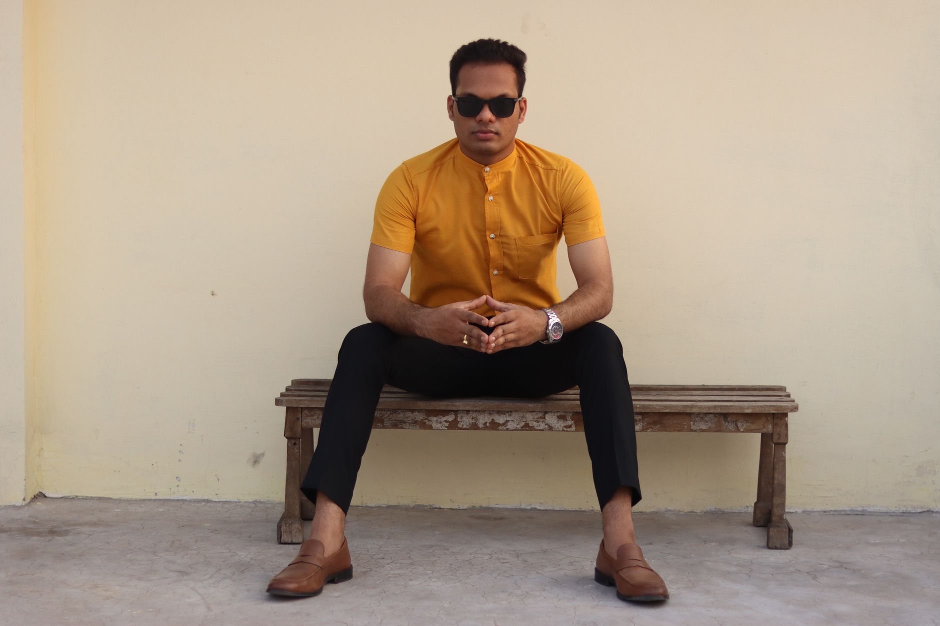 A man in sunglasses and a yellow shirt sits confidently on a wooden bench.