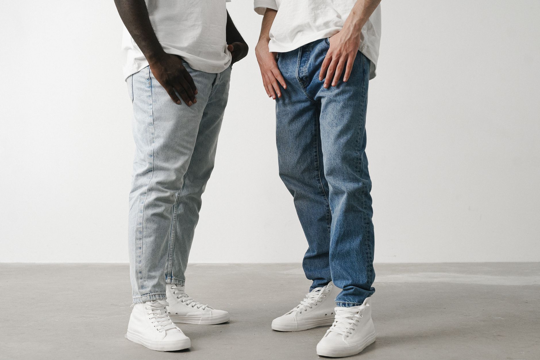 Close-up of two individuals wearing jeans and white sneakers in a minimalist setting.