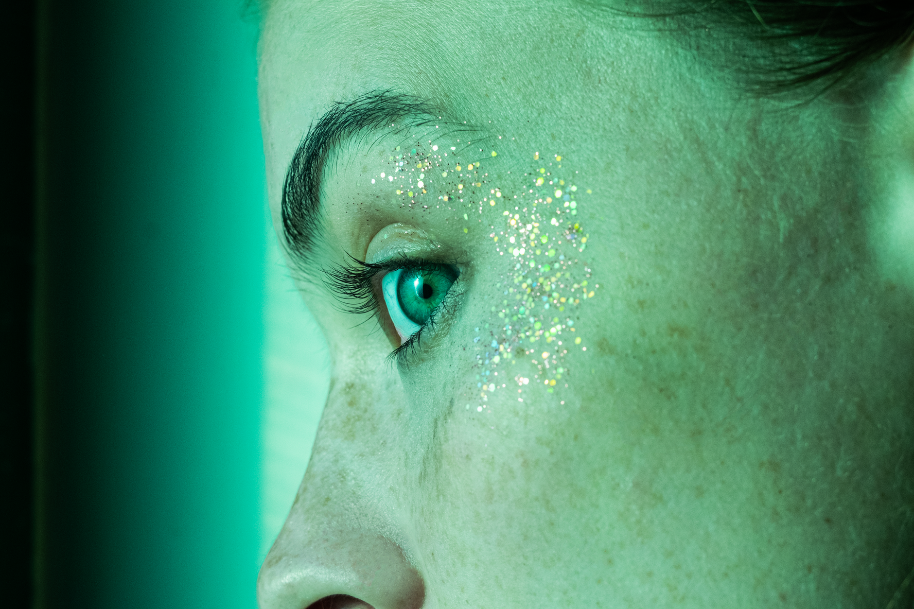 Close-up of a person's eye adorned with glitter, bathed in a vibrant green light.