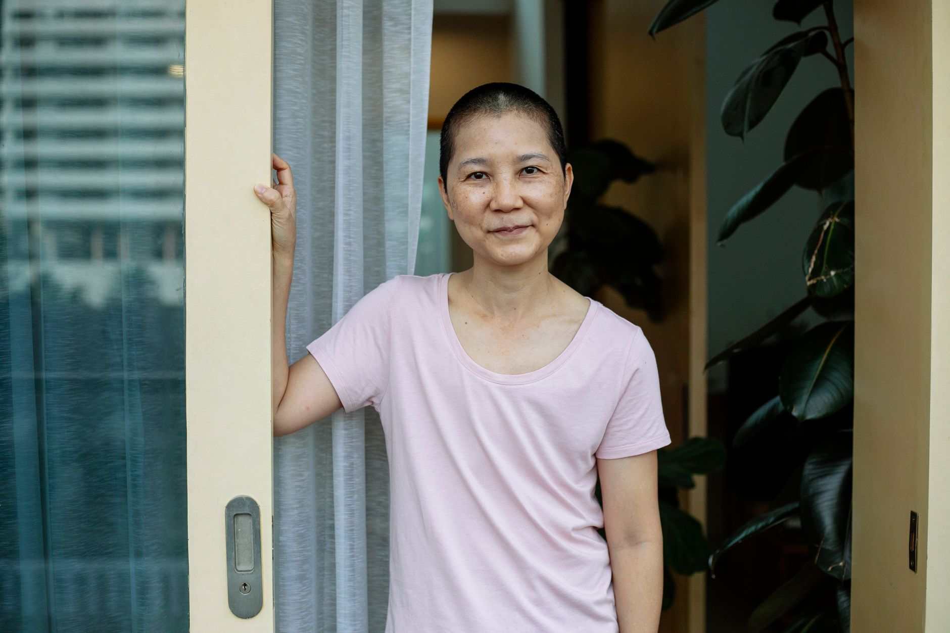 Positive middle aged Asian female with short dark hair in casual clothes standing near door of terrace and looking at camera