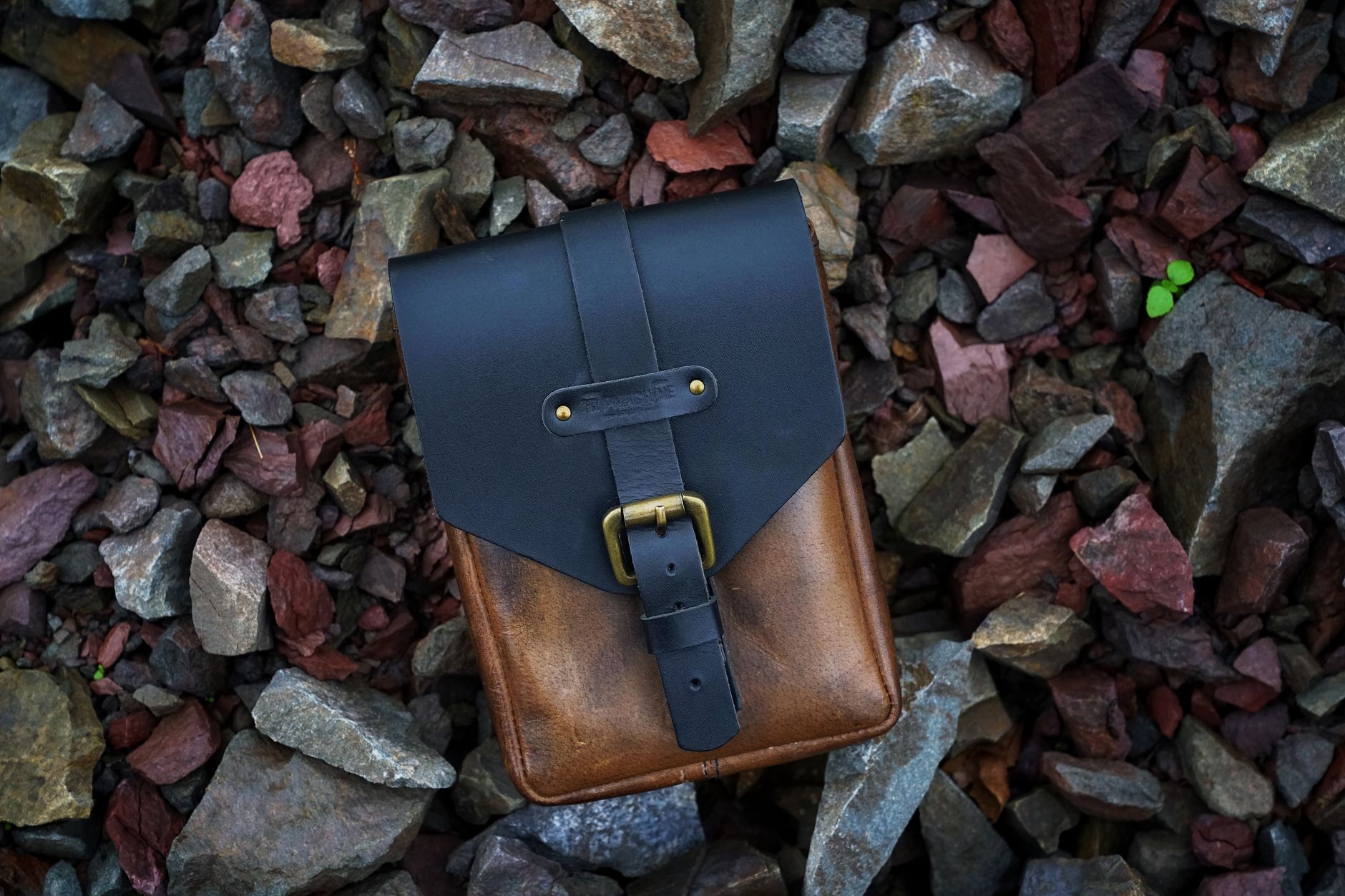 Stylish black leather bag placed on colorful rocks, showcasing chic fashion.