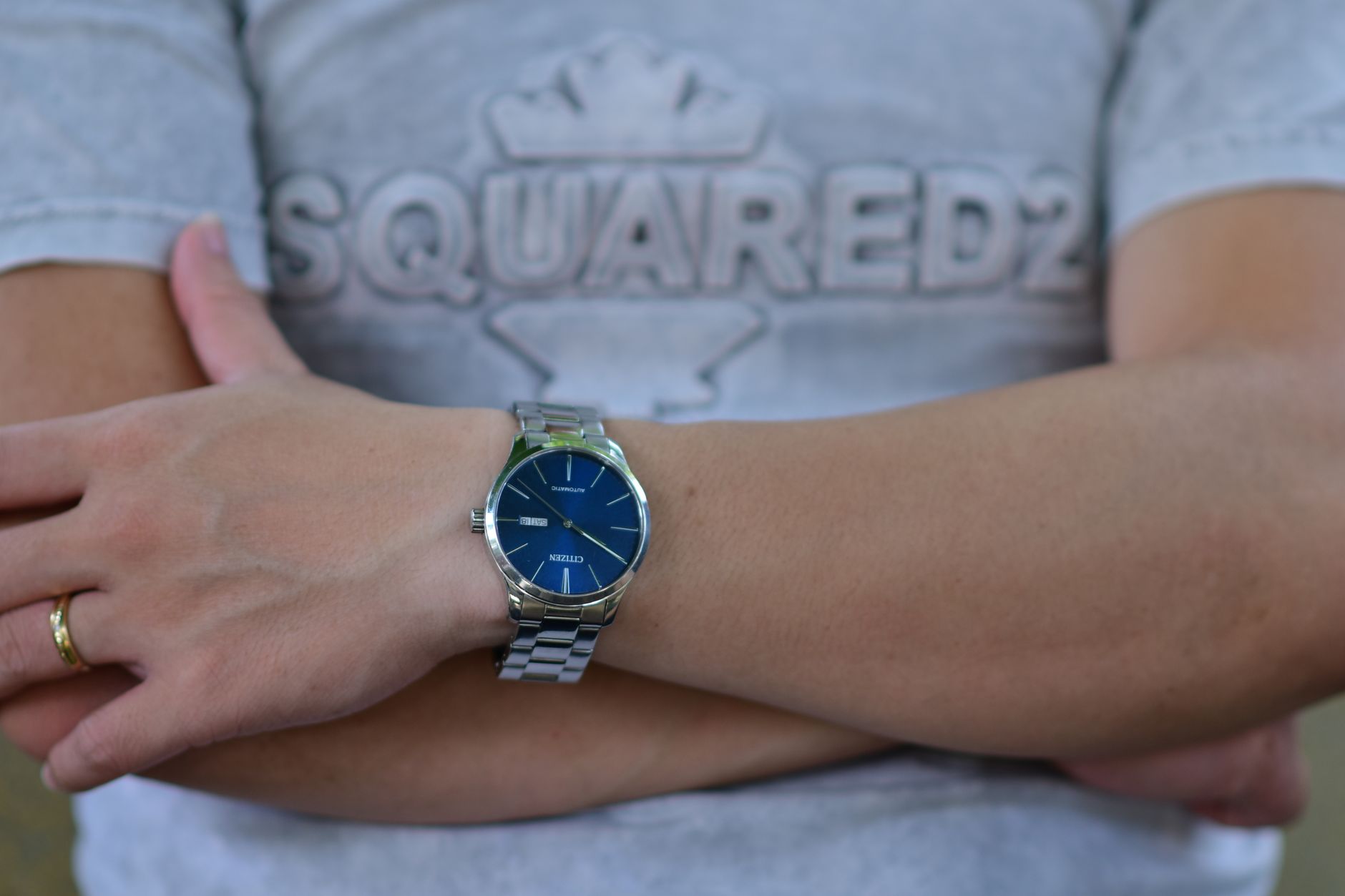 Close-up of a stylish wristwatch with a blue dial worn on crossed arms.