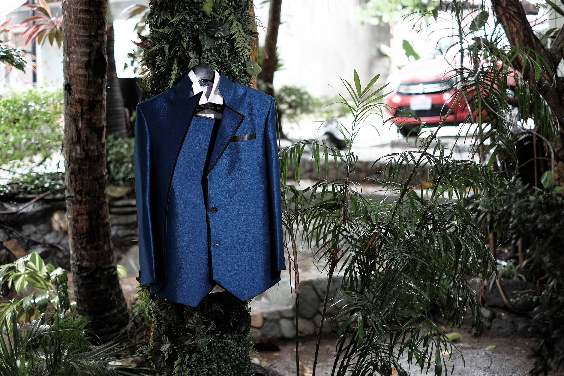 A stylish blue suit elegantly hangs on a tree outdoors, surrounded by lush greenery.