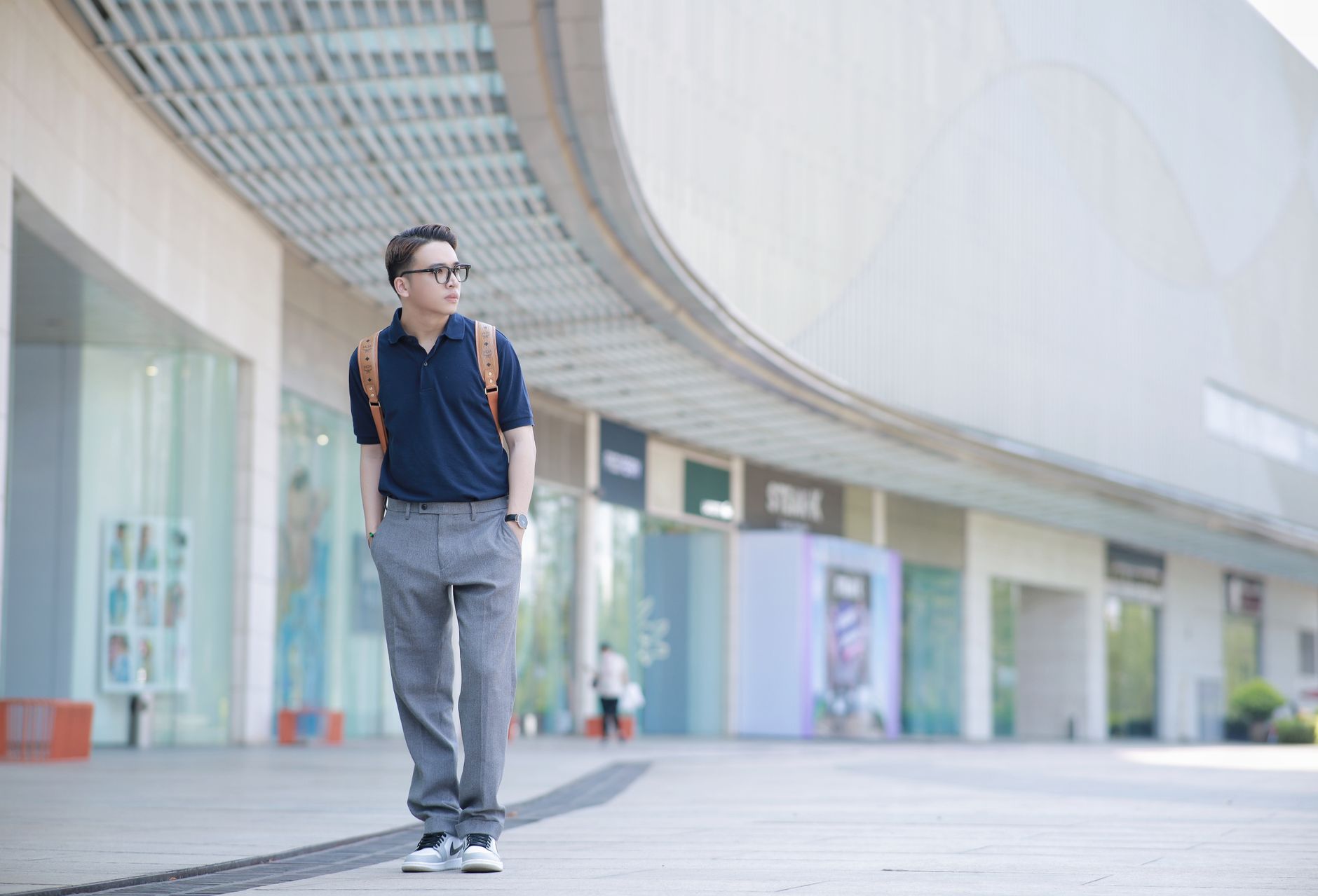 Fashionable man posing in city setting, wearing blue shirt and backpack. Urban lifestyle vibe.