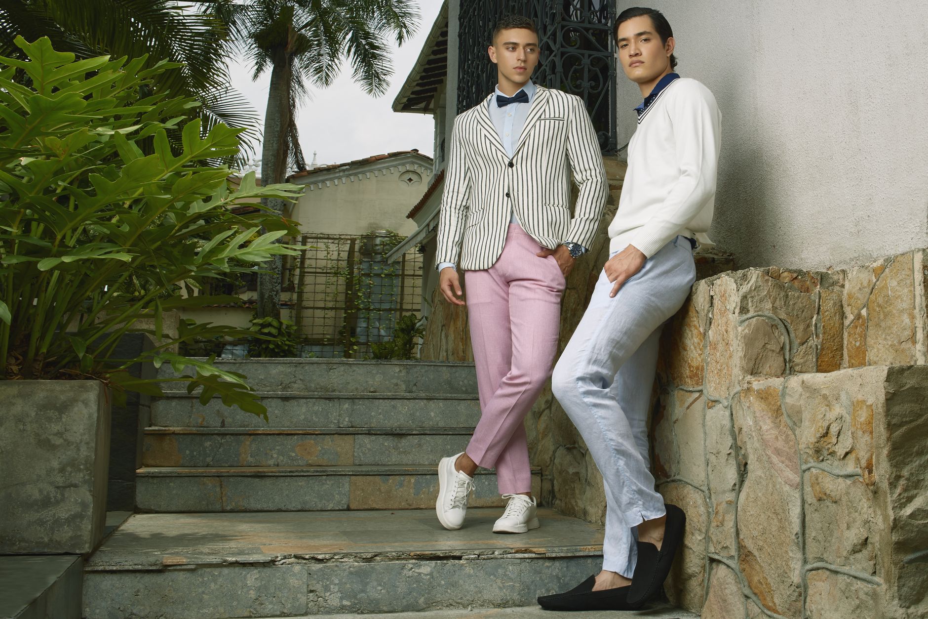 Two stylish young men posing in fashionable attire in an outdoor setting in Colombia.