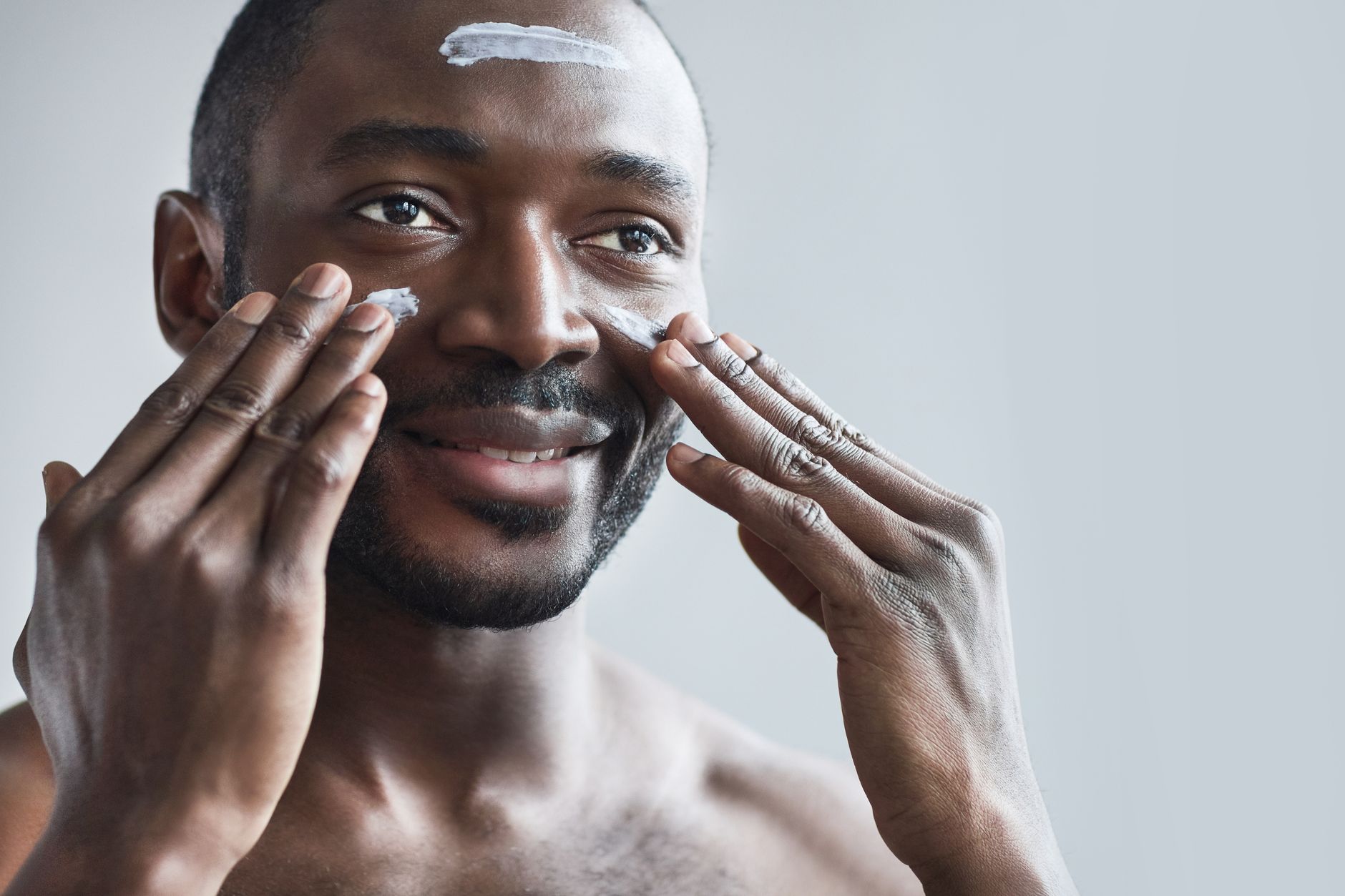 Smiling man applying face cream as part of his daily skincare routine for healthy skin.