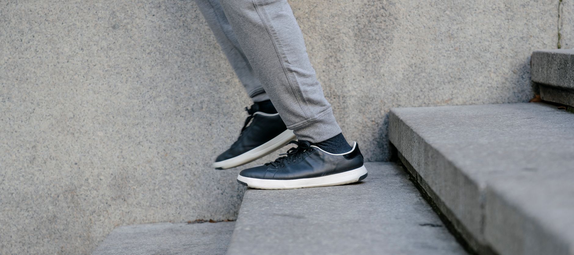 Crop unrecognizable male in trendy black sneakers and gray sporty pants descending down staircase in park in morning