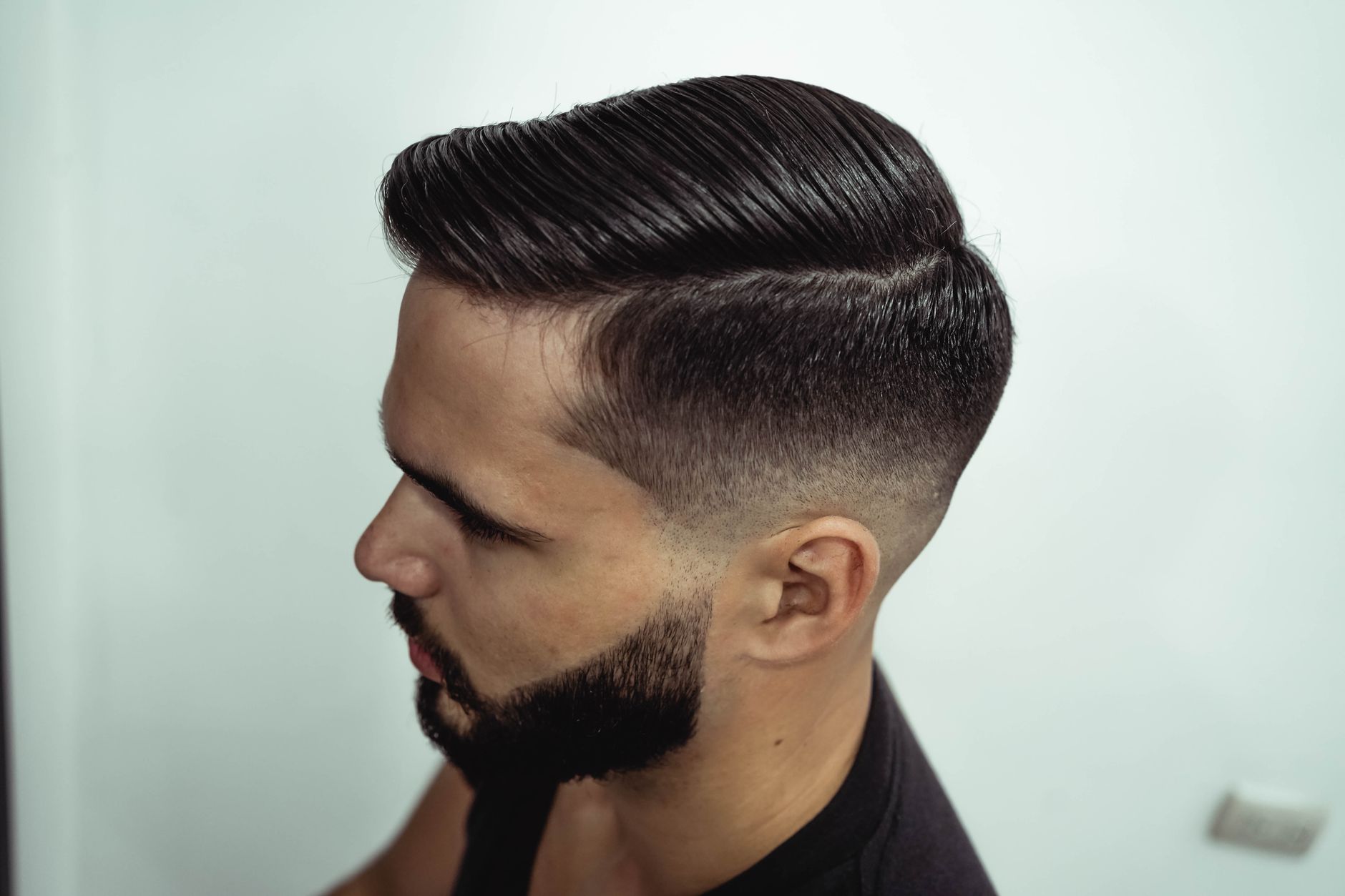 Close-up shot of a man's stylish haircut and beard, showcasing grooming precision.