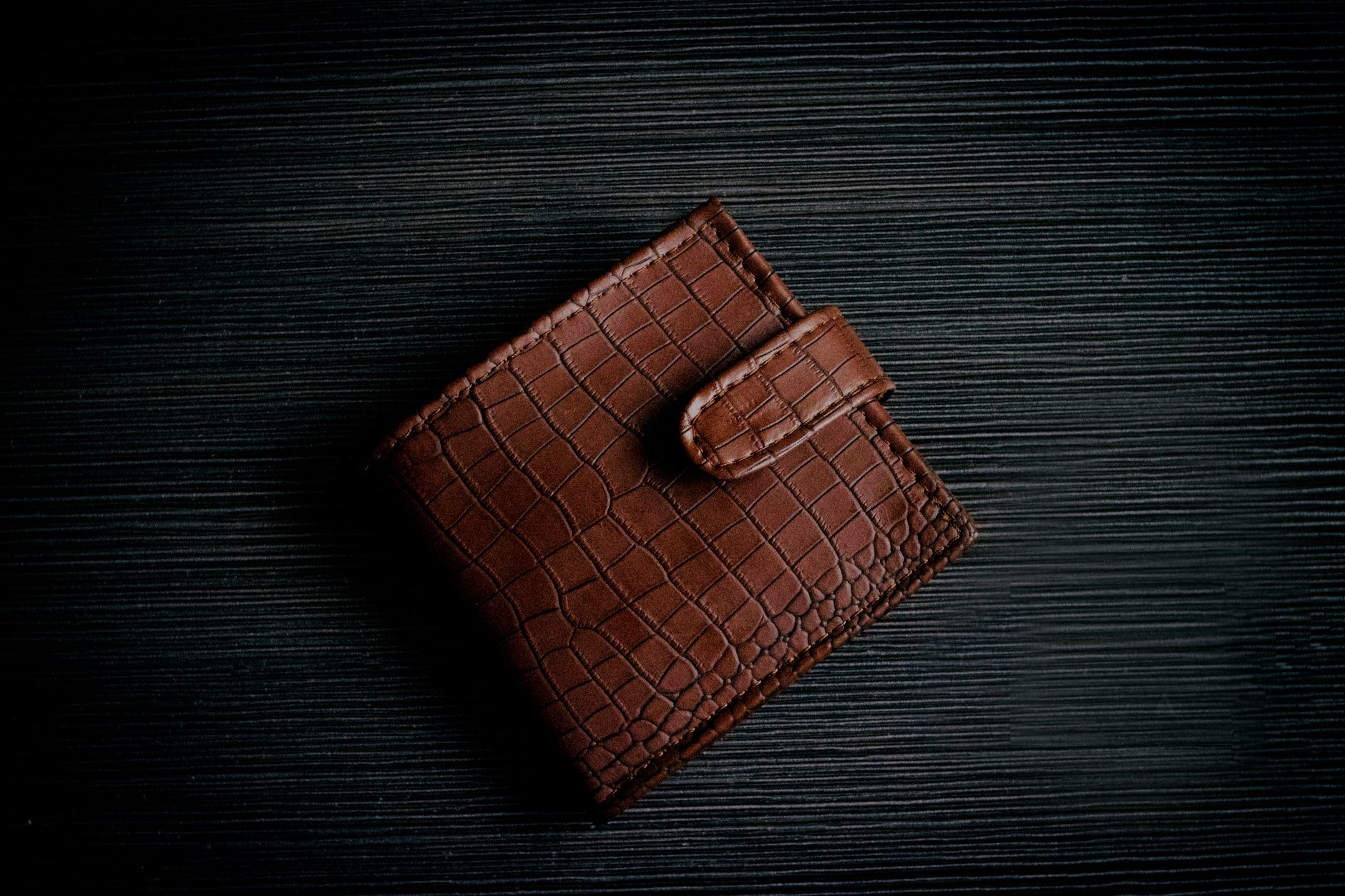 A stylish brown leather wallet with a textured design lies on a dark surface, showcasing its elegant craftsmanship.