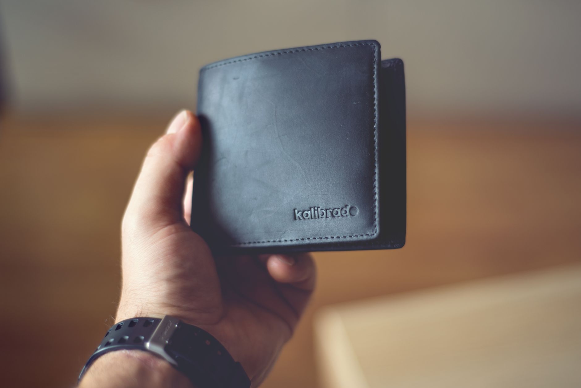 Close-up of a stylish black leather wallet held by a person, showcasing design.