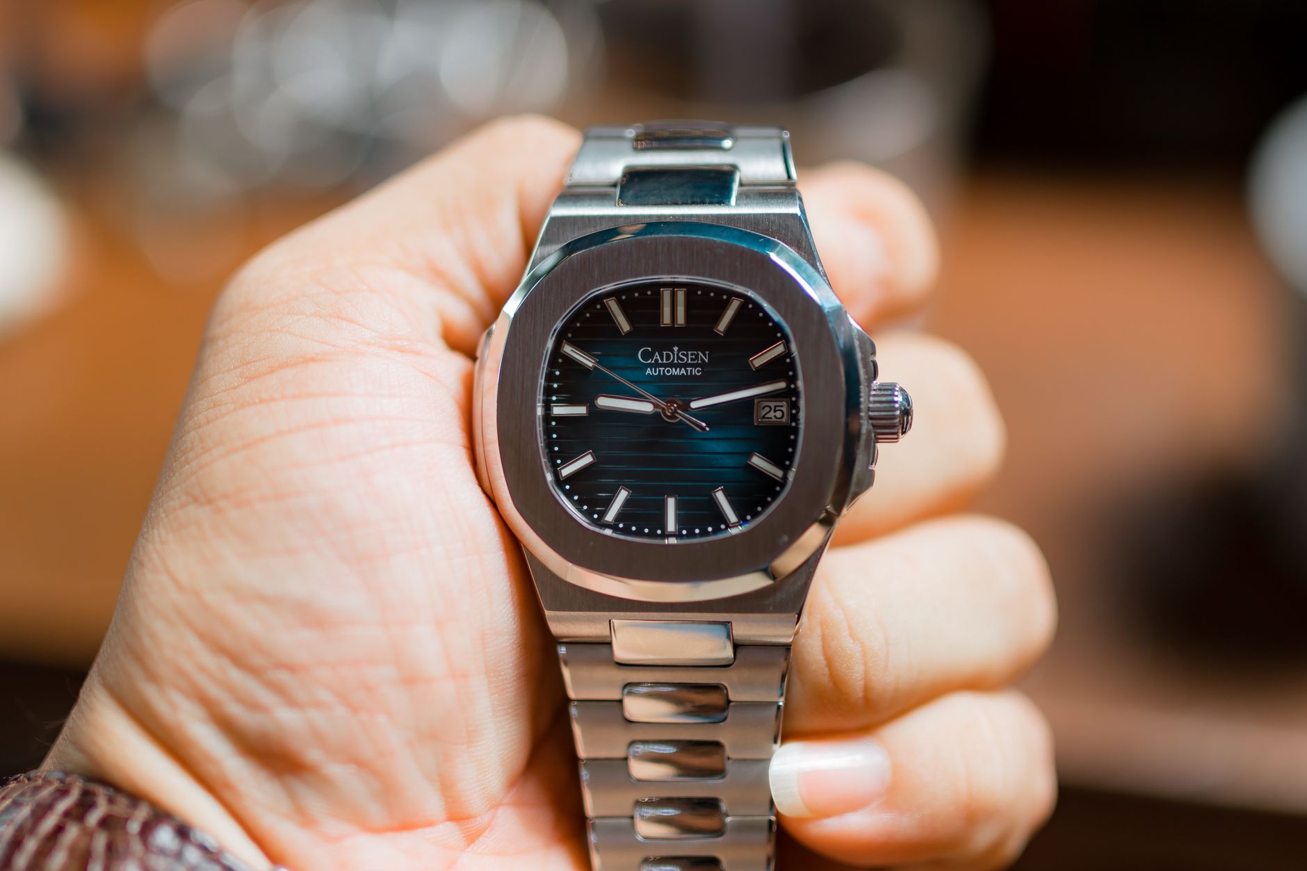 Close-up of a metallic wristwatch being held, showcasing its sleek design.
