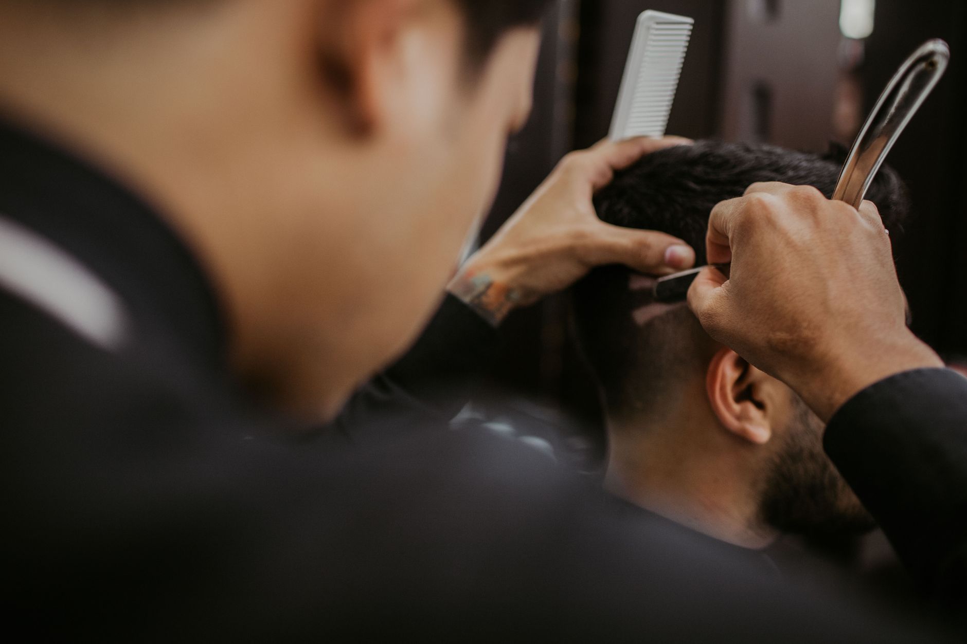 Close-up of a barber expertly styling a man's hair with a razor and comb in a trendy barbershop.