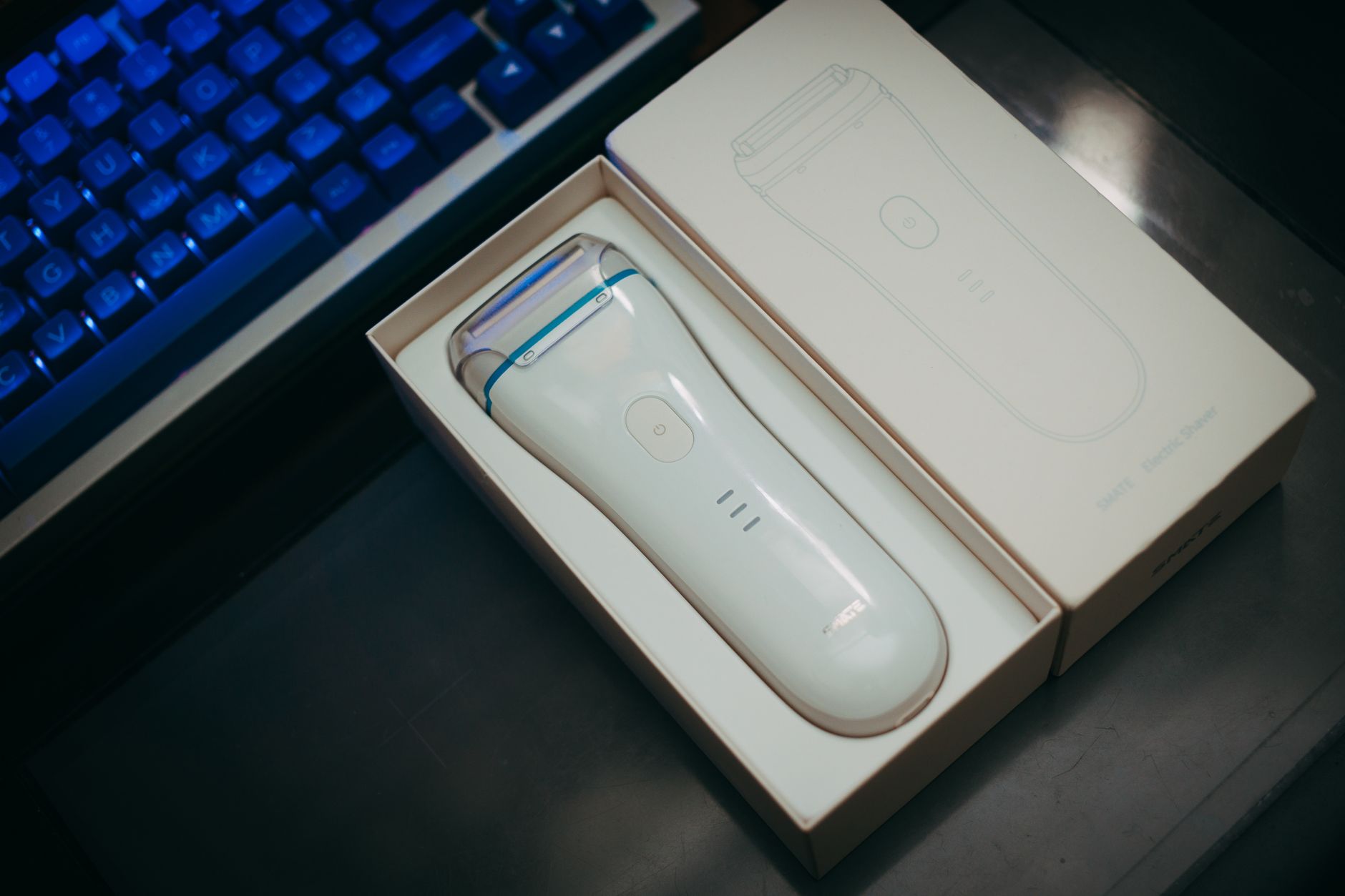 White electric shaver in elegant box beside keyboard on a dark surface.