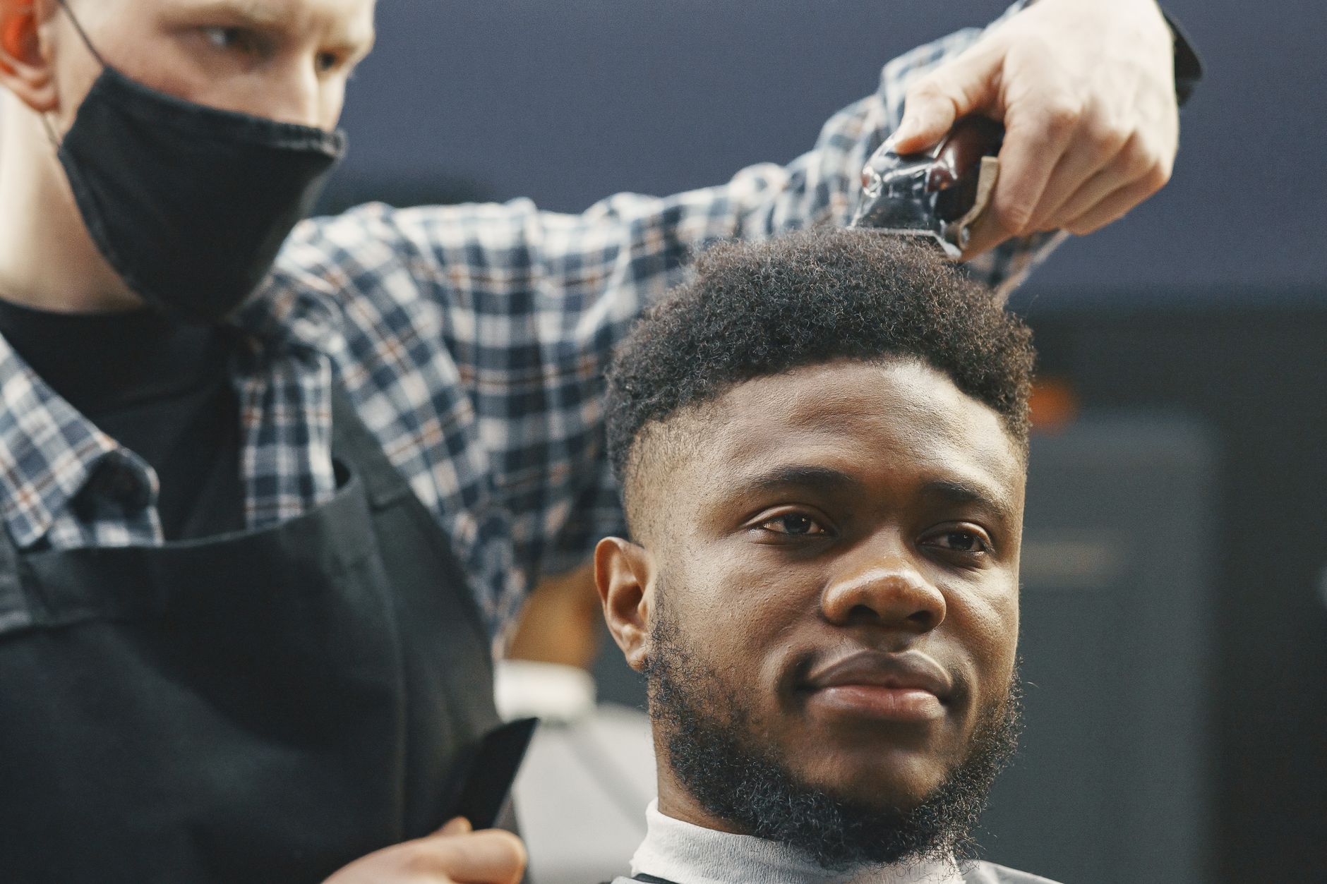 A barber trims a smiling man's hair using clippers in a professional setting.
