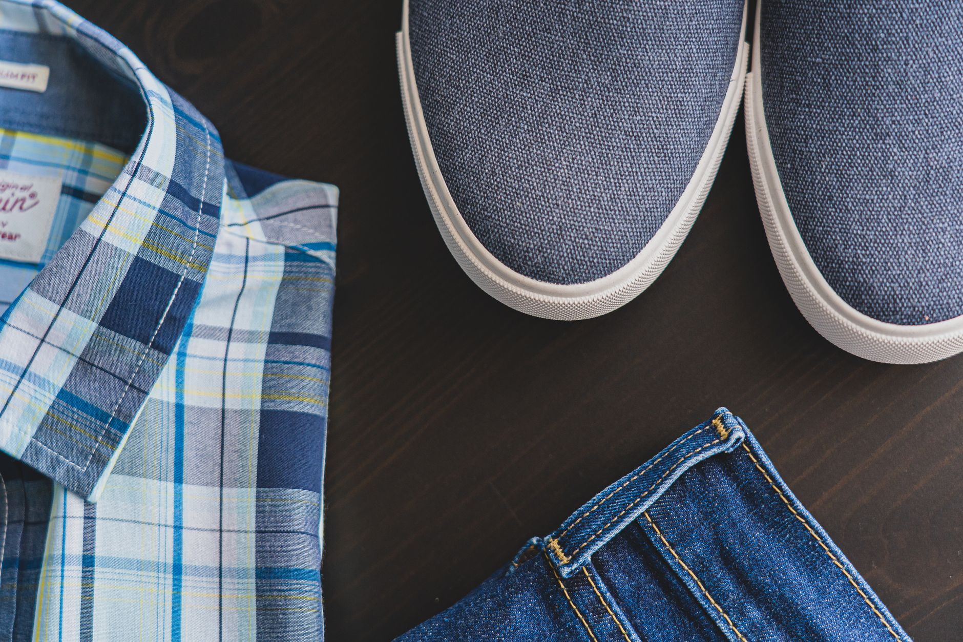 Flat lay of a casual men's outfit with checkered shirt, denim jeans, and blue sneakers.