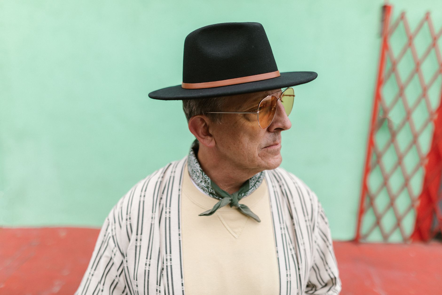Elderly man in chic outfit and hat poses against a colorful urban backdrop, exuding style and confidence.