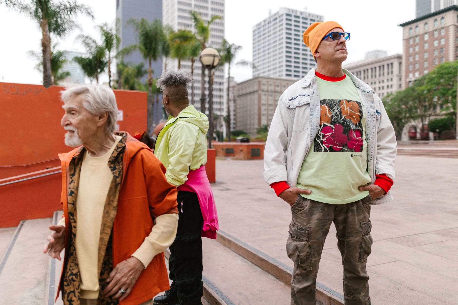 Three stylish individuals in colorful attire, showcasing urban street fashion in a city square.