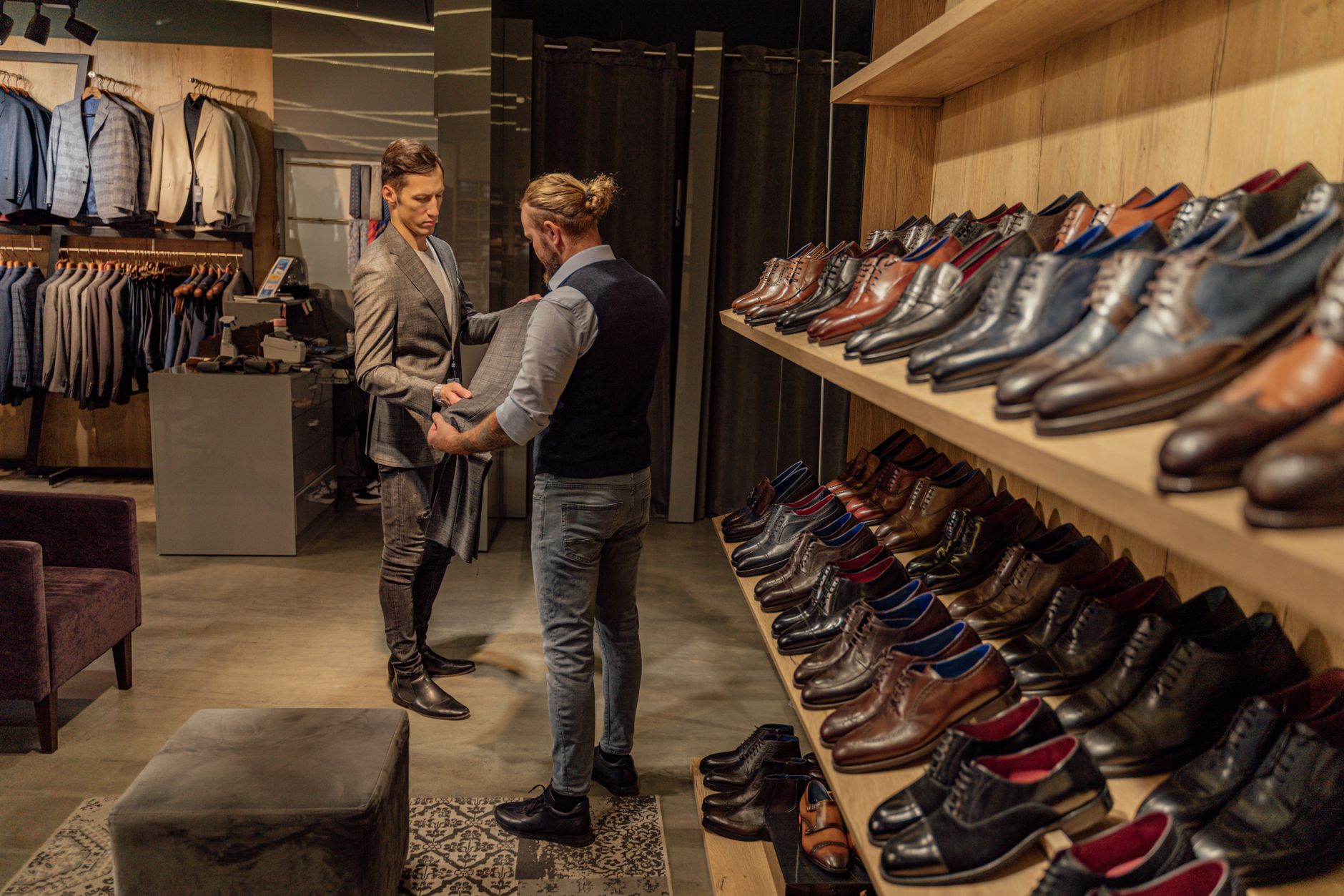 Two men shopping in a stylish clothing store with a wide range of shoes and suits displayed.