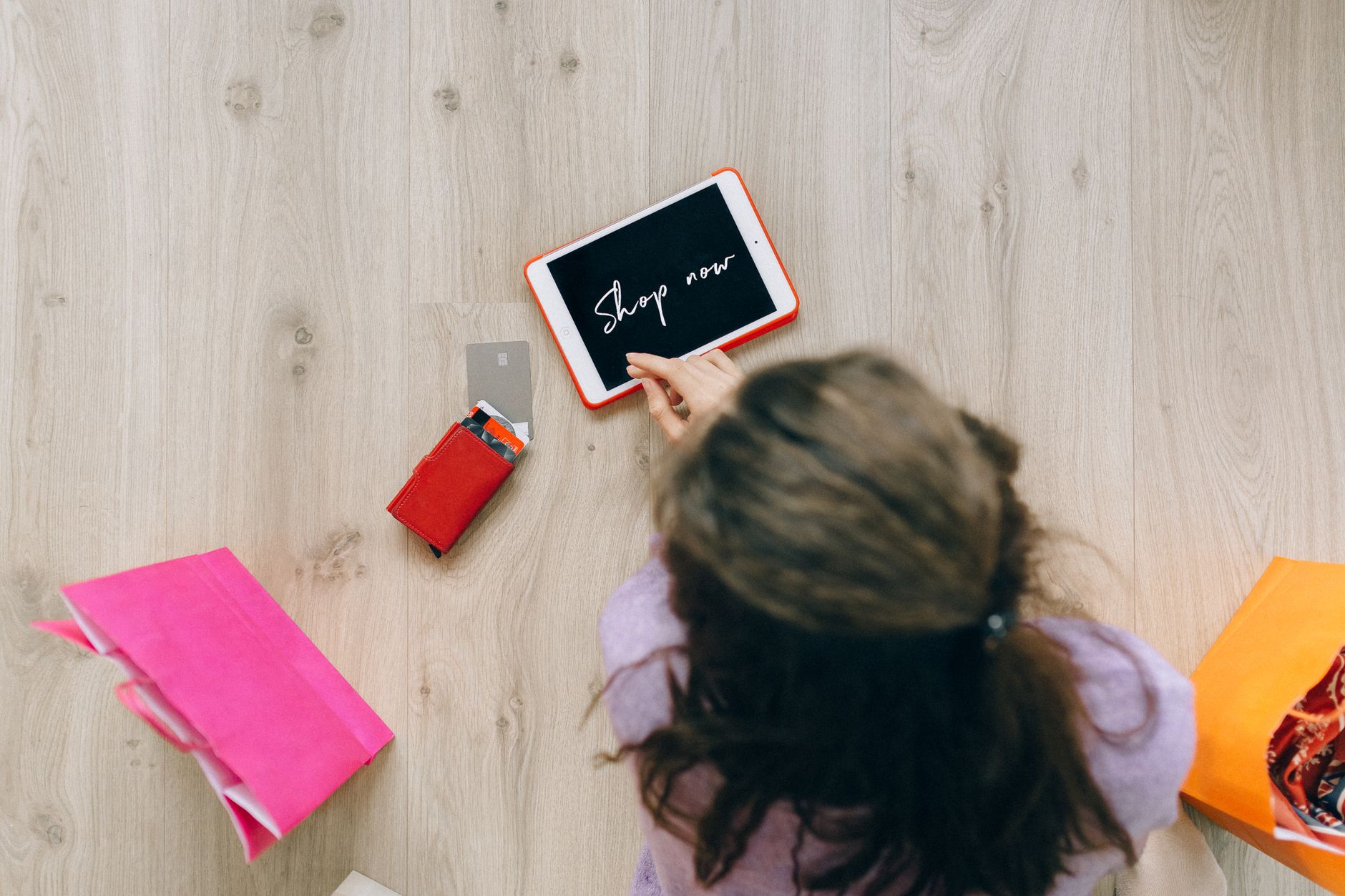 Overhead view of a woman using a tablet for online shopping surrounded by shopping bags and cards.
