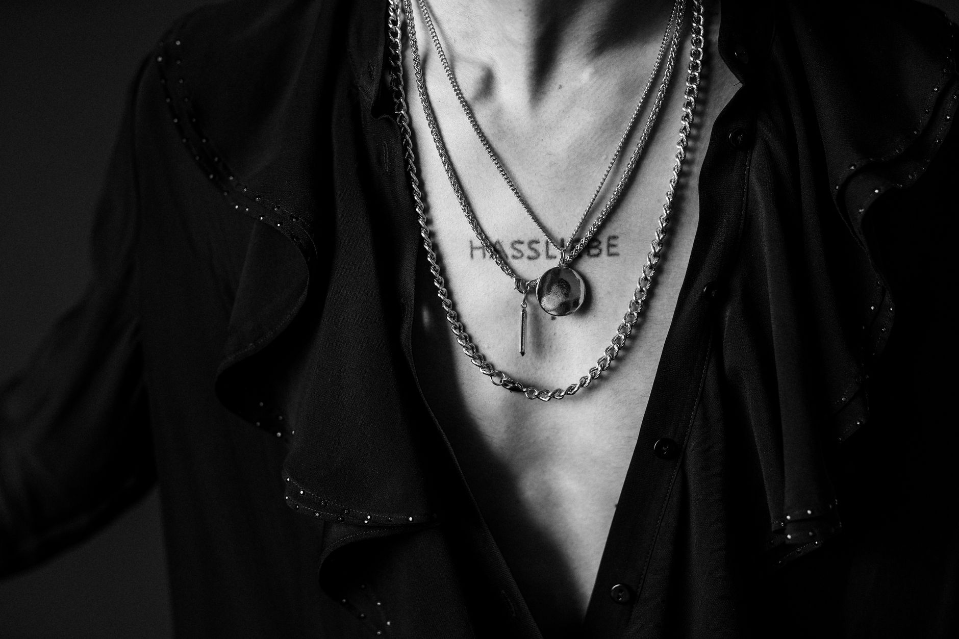 Black and white close-up of stylish layered necklaces with a tattoo.