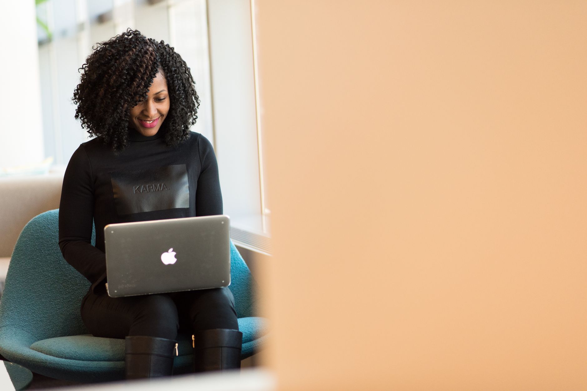 African American woman happily working on a laptop in a modern office setting.