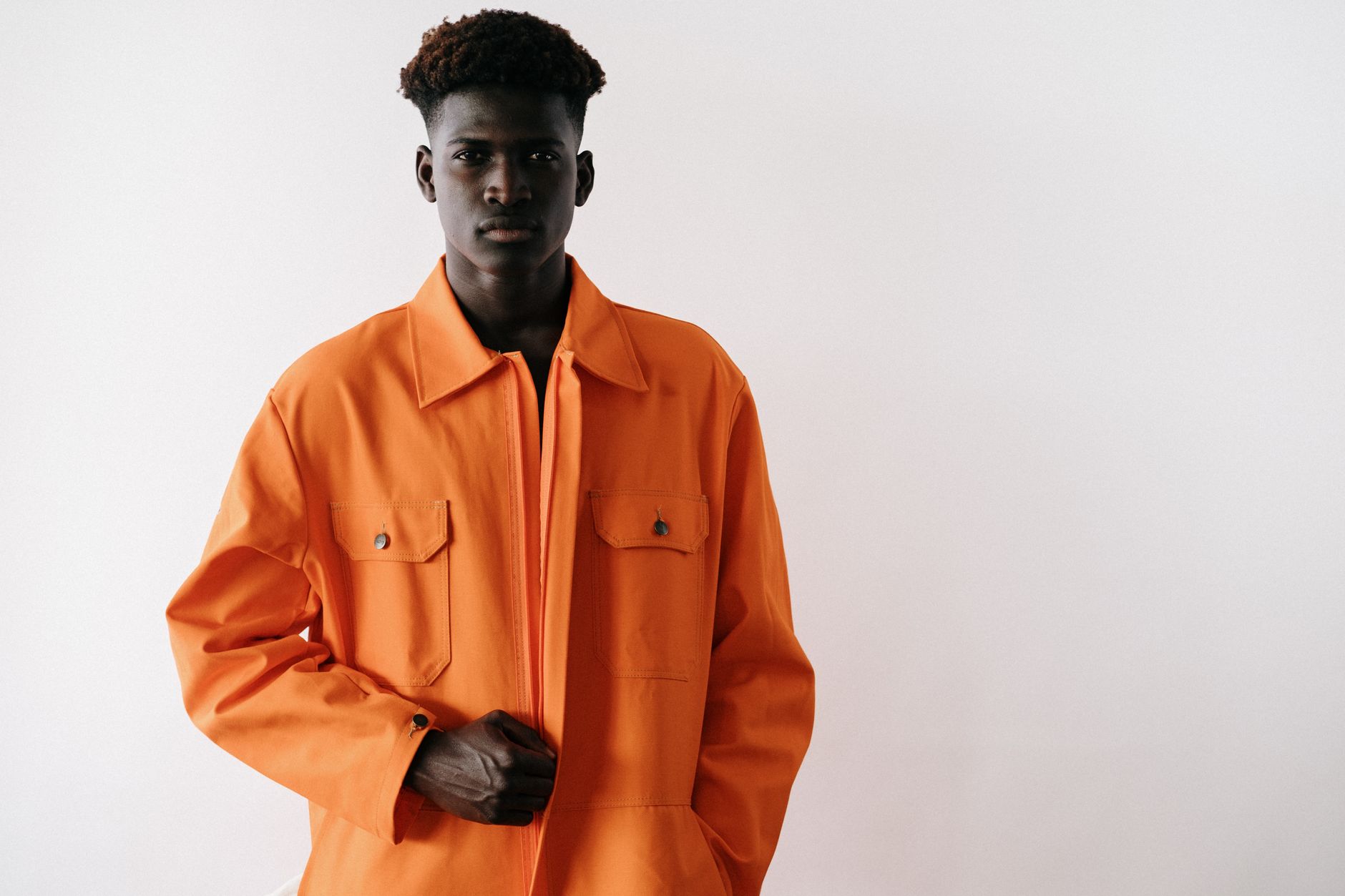 Portrait of a black man in stylish orange workwear posed against a white backdrop during a studio shoot.