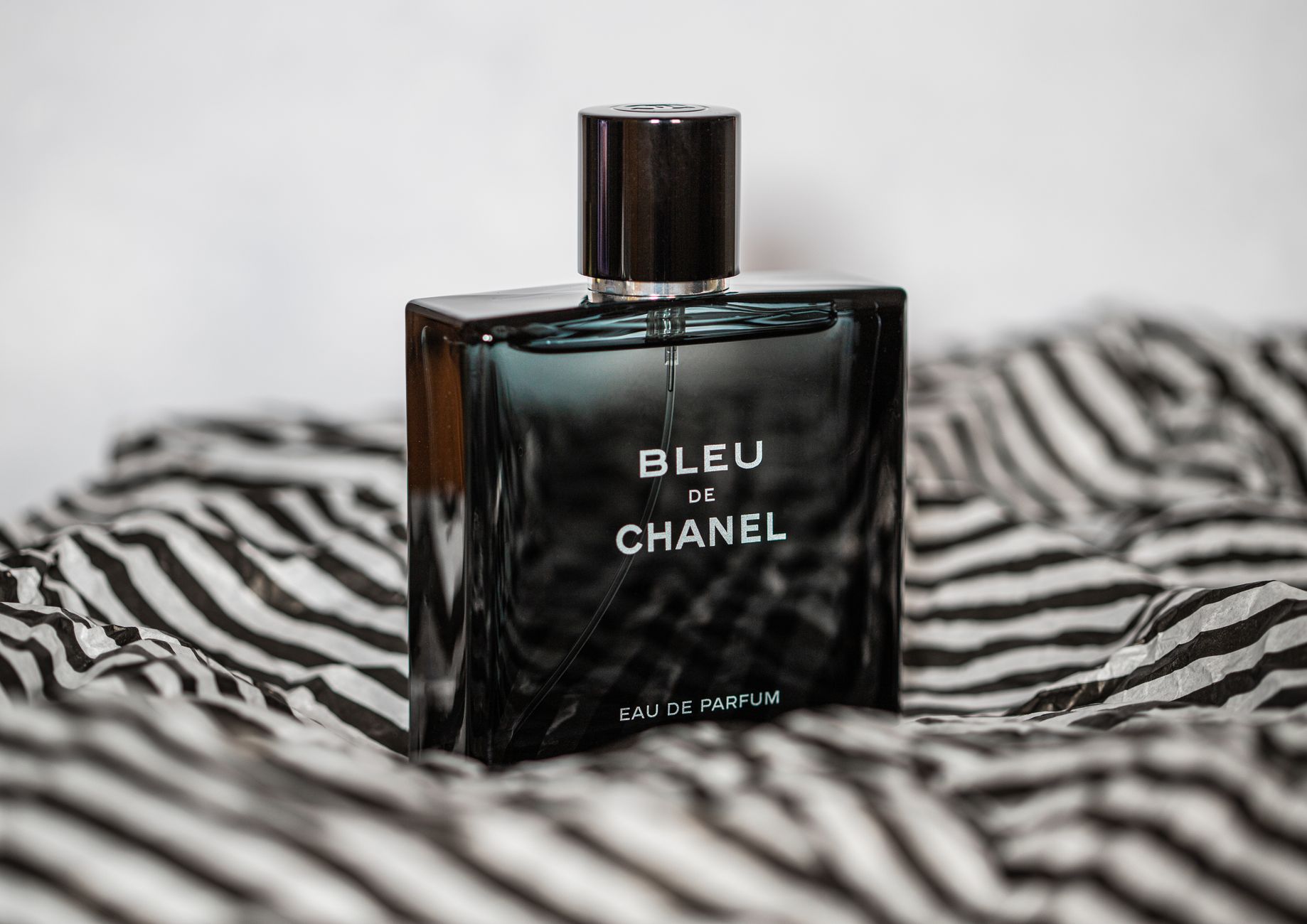 Elegant product shot of Bleu de Chanel perfume on striped fabric conveying luxury and sophistication.