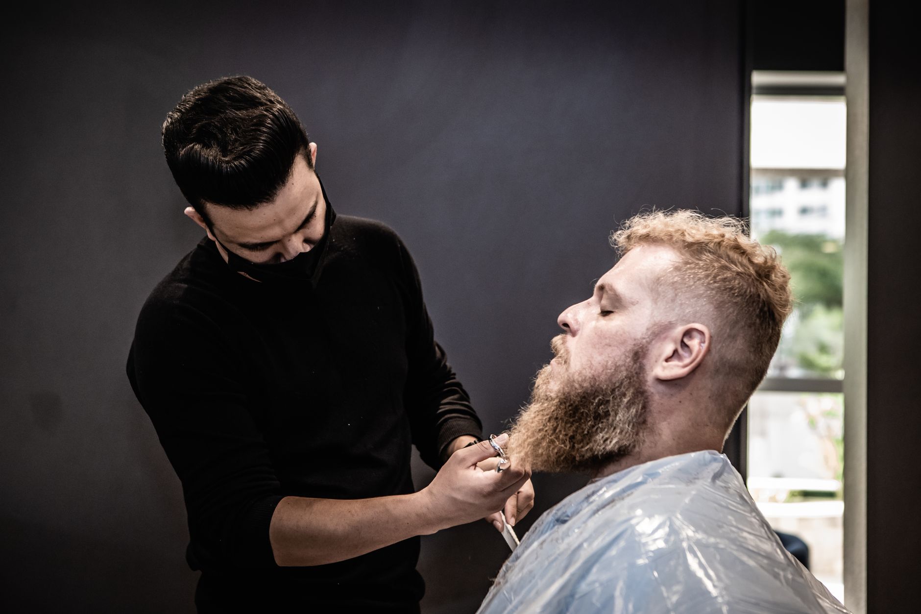 A barber professionally trims a man's beard in a modern salon.