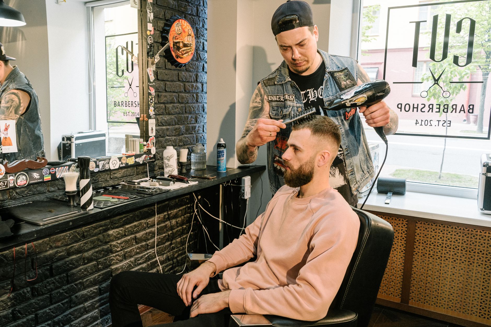 Barber styling a man's hair with a blow dryer in a contemporary barbershop setting.
