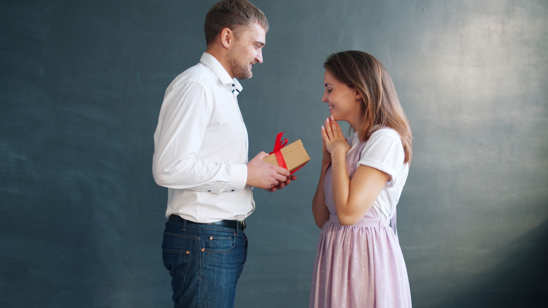 A cheerful couple exchanging a gift with a red ribbon, celebrating a special occasion.