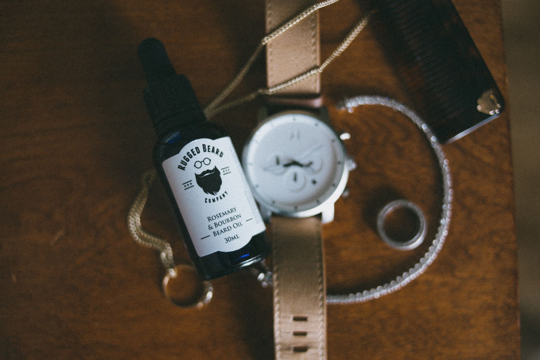 Stylish flatlay featuring beard oil, watch, and jewelry on a wooden table.