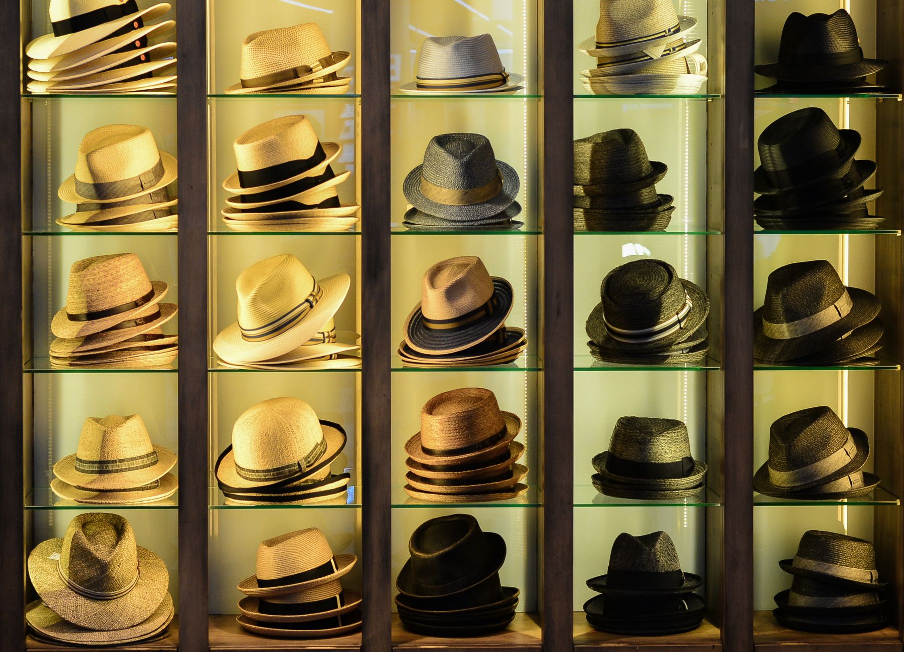 A stylish assortment of hats in various designs and colors showcased on glass shelves.