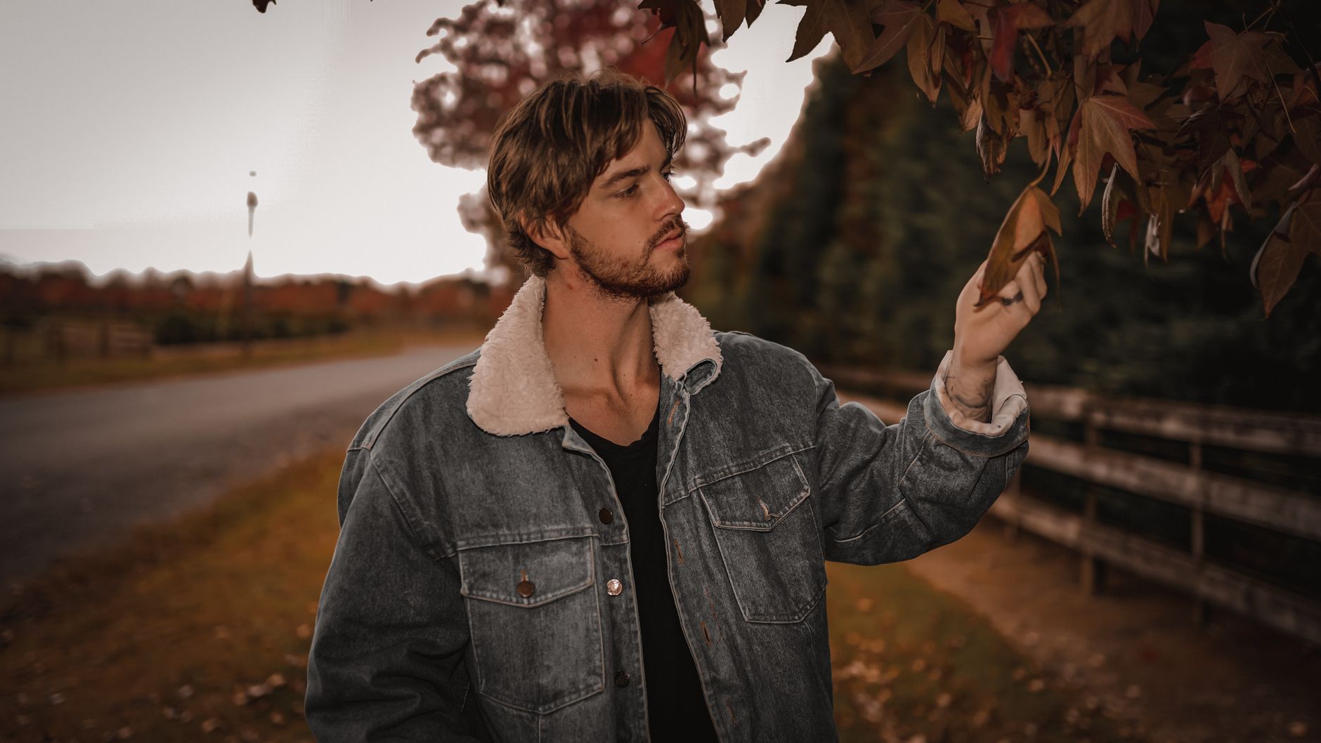 Man in a denim jacket admiring autumn leaves, capturing the essence of fall outdoors.