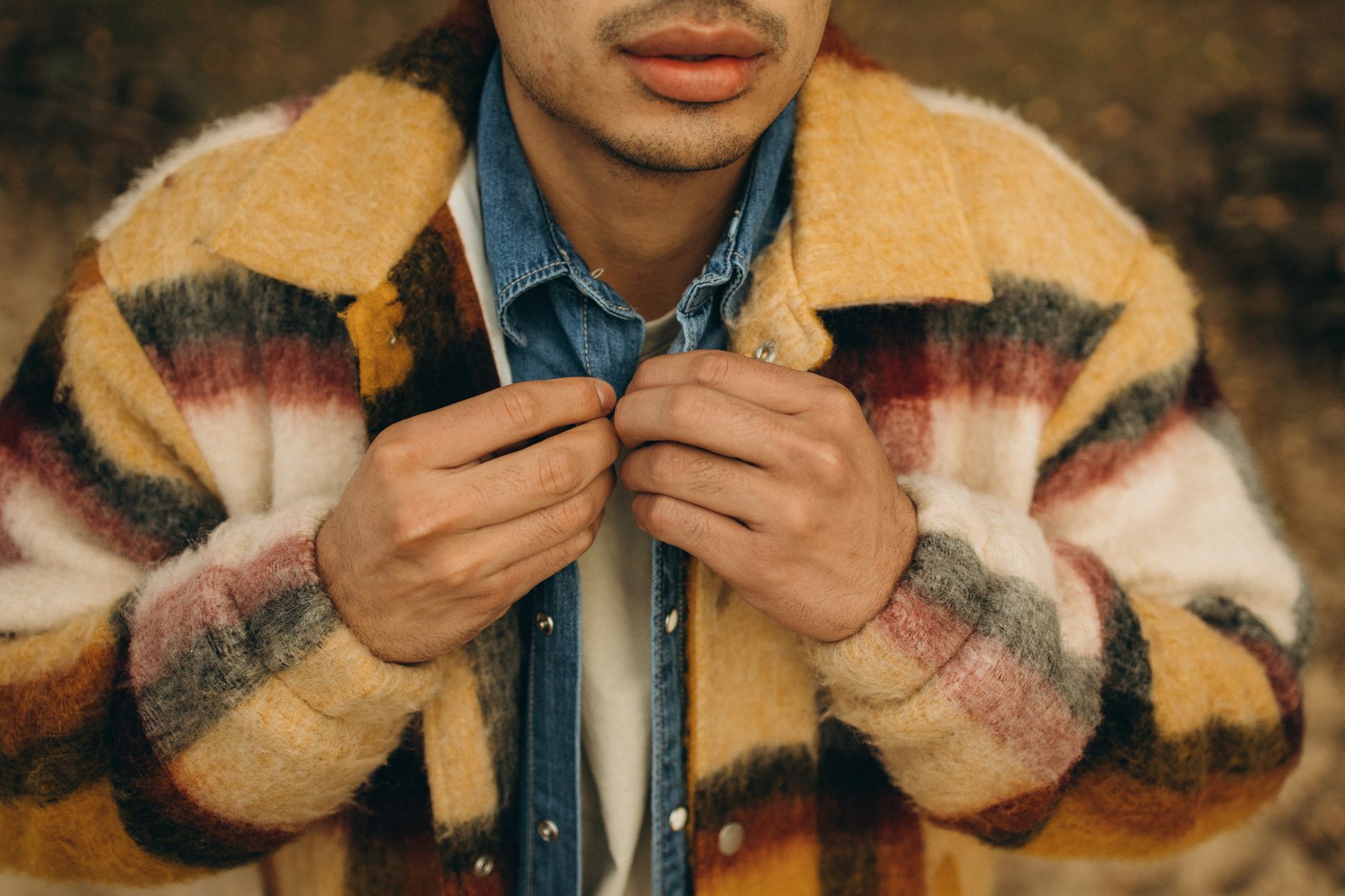 A detailed close-up of a man adjusting his checkered coat outdoors during fall.