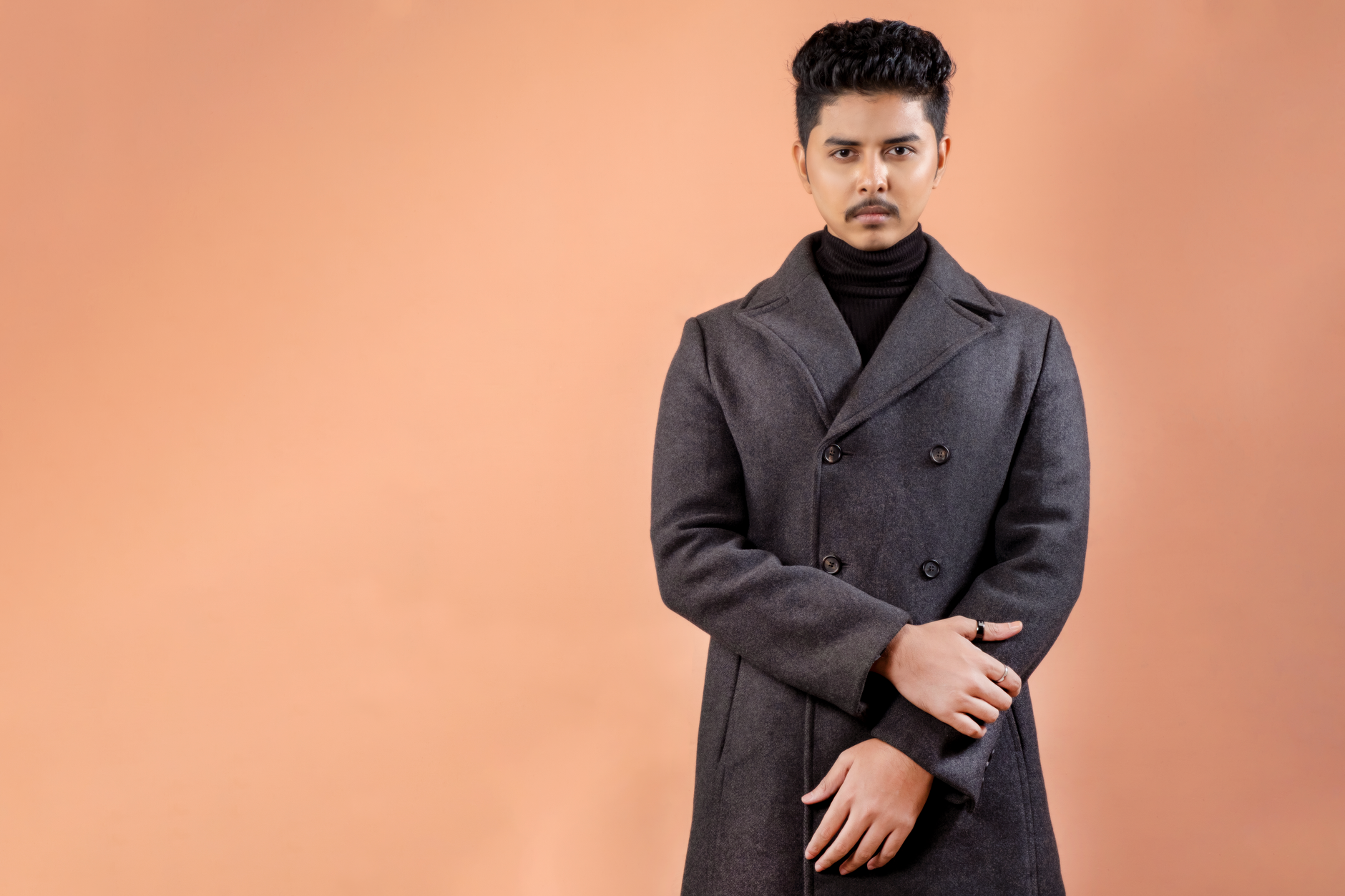 Sophisticated portrait of a man wearing a gray overcoat against a warm backdrop.